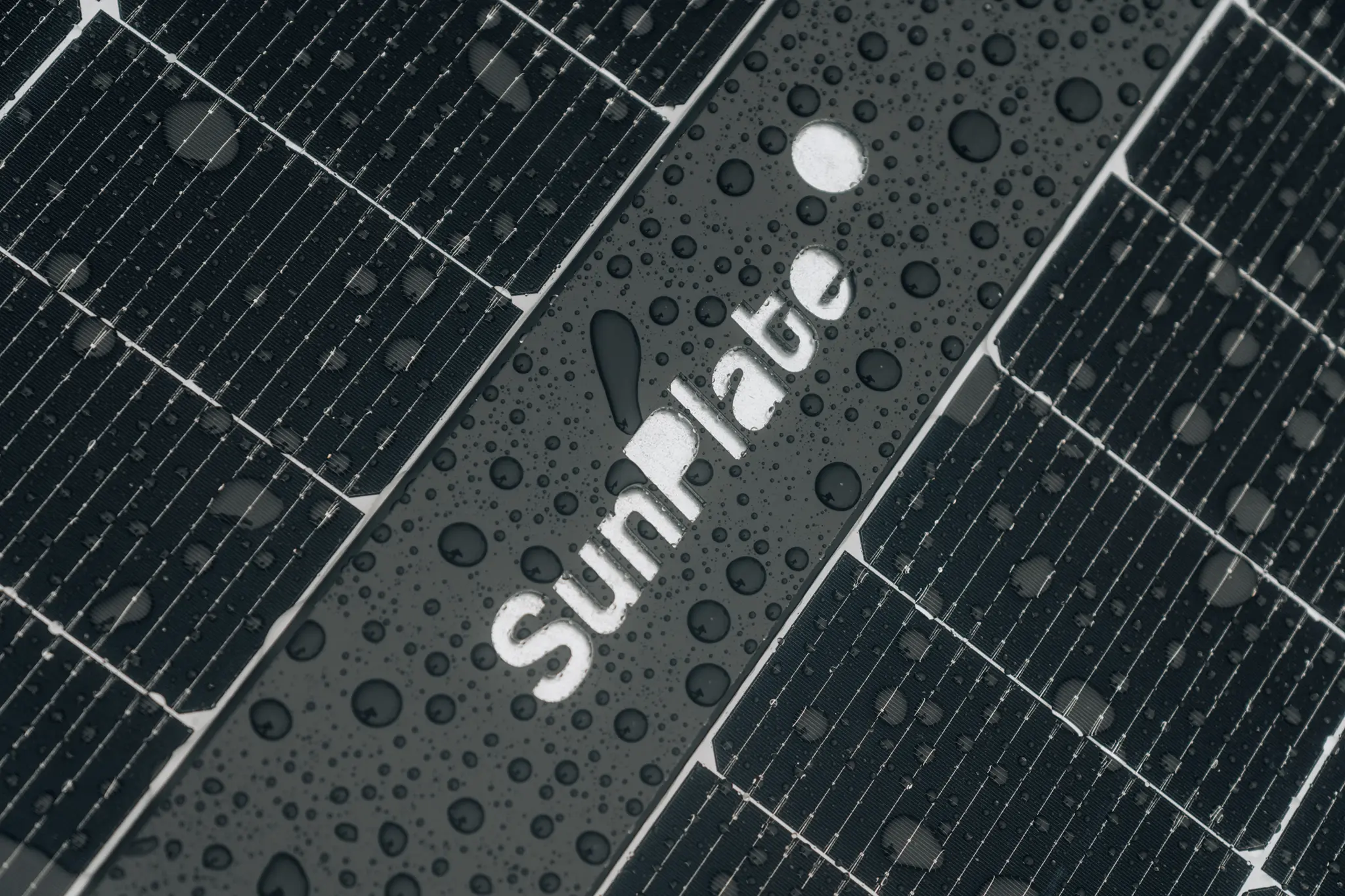 Nahaufnahme regennasser Solarmodule mit zahlreichen Wassertropfen und dem weißen Schriftzug „SunPlate“ auf einem dunklen Mittelsteg.